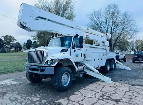 A white bucket truck with its outriggers down on a paved lot