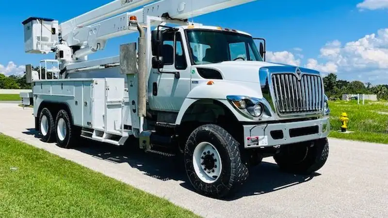 A white bucket truck with an aerial boom parked beside a green lawn