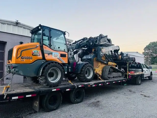 Two loaders strapped on a trailer behind a pickup at sunset